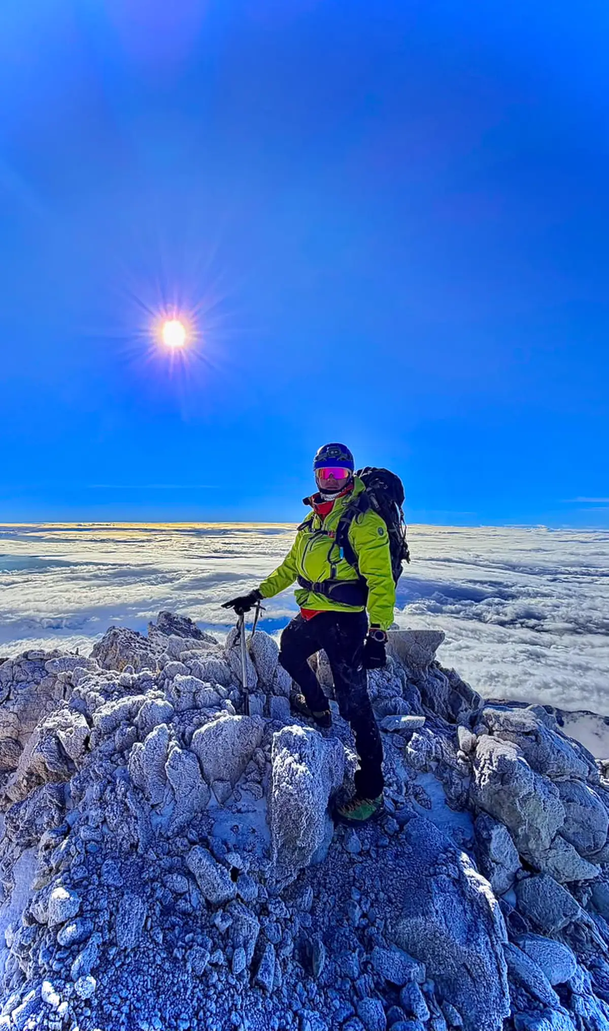 Martín en la cumbre, sobre roca escarchada y con el sol de frente.
