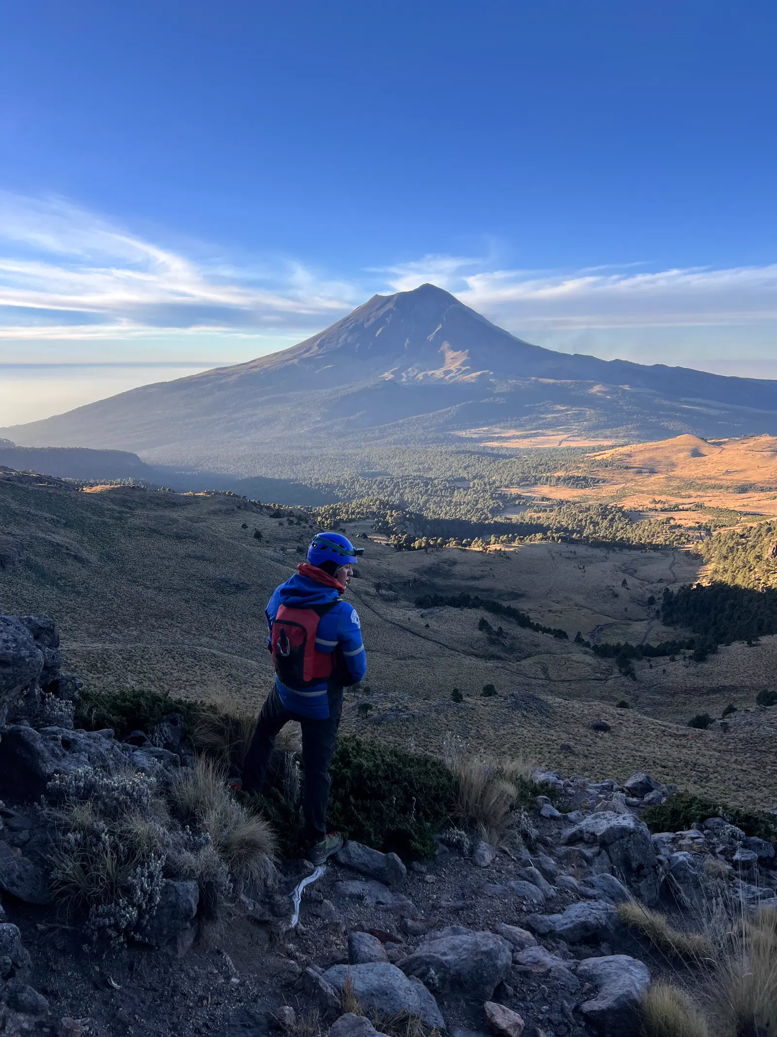 Excursionista mirando un volcán desde un mirador, con el valle de fondo.