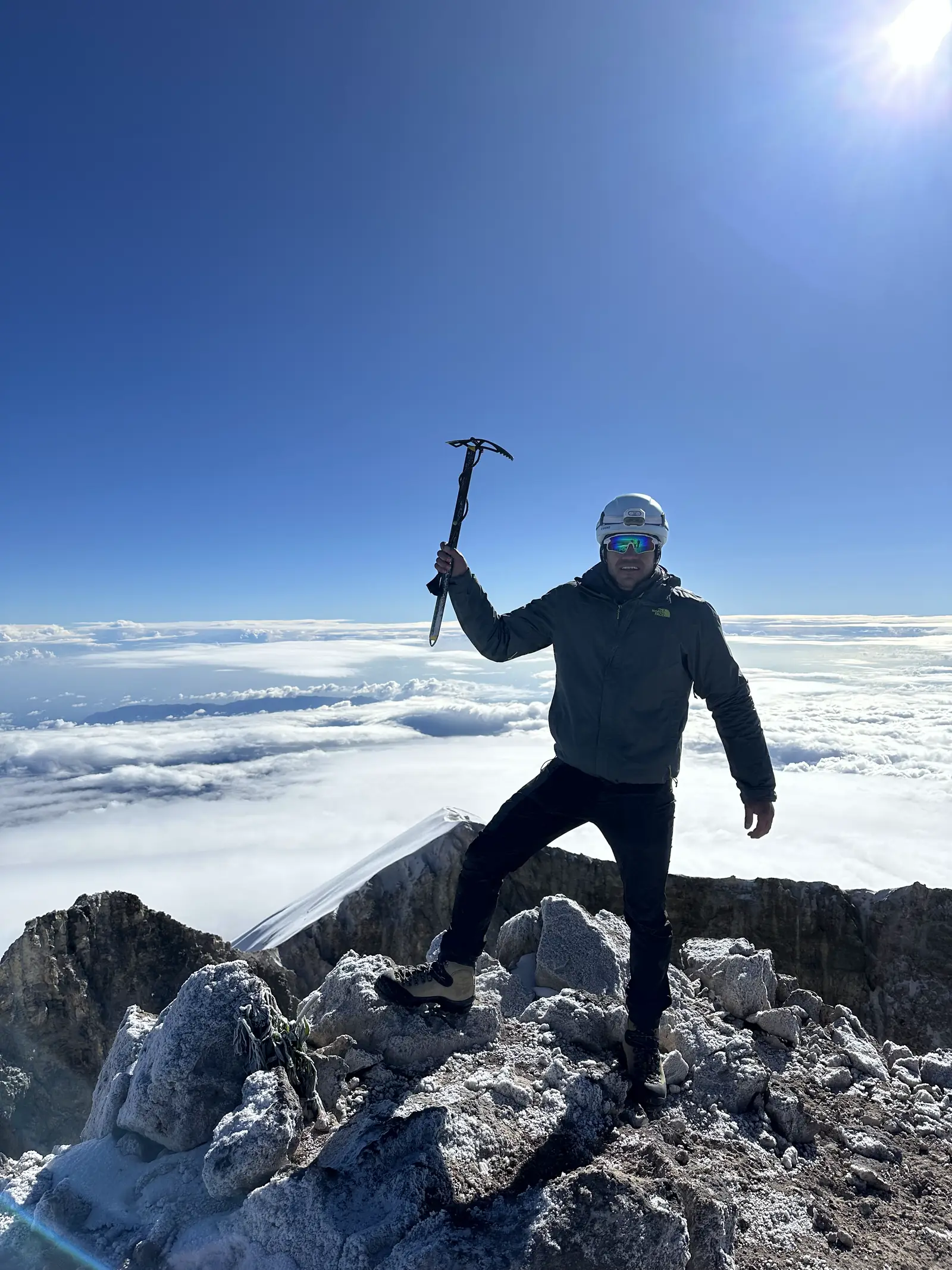 Montañista a contraluz con el piolet en alto sobre el mar de nubes, en la cumbre del Pico de Orizaba.