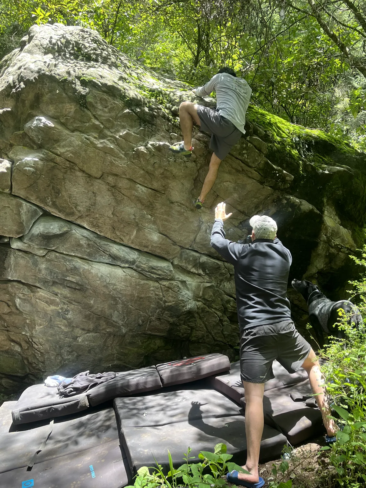 Escalador saliendo por arriba de un bloque de roca en Salazar mientras un compañero lo cuida desde la colchoneta.